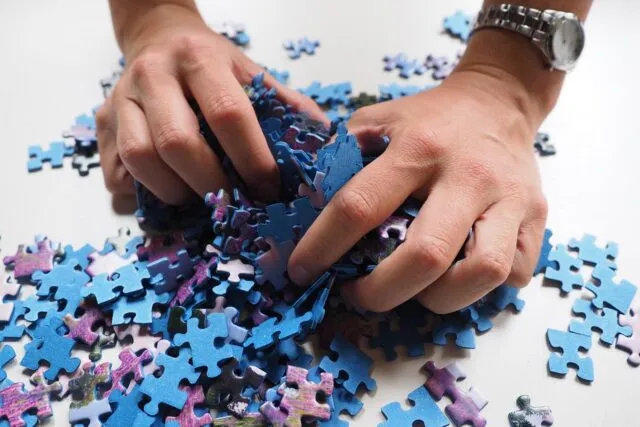 Masă de living cu un puzzle început, piese sortate pe margini și o lampă aprinsă alături